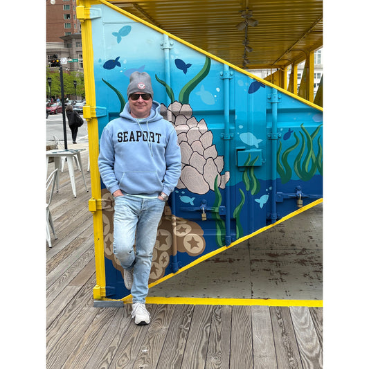 Man in light blue hoodie with SEAPORT TEXT, BEANIE AND SUNGLASSES