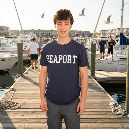 Person wearing a navy blue 'SEAPORT' t-shirt standing by a marina.