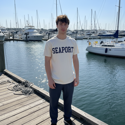 Person wearing a 'Seaport' t-shirt standing on a dock with marina background