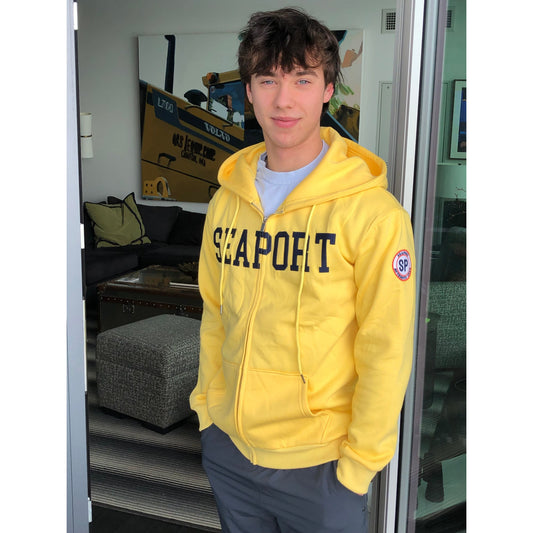 Man with hands in pocket in a yellow hoodie that says seaport