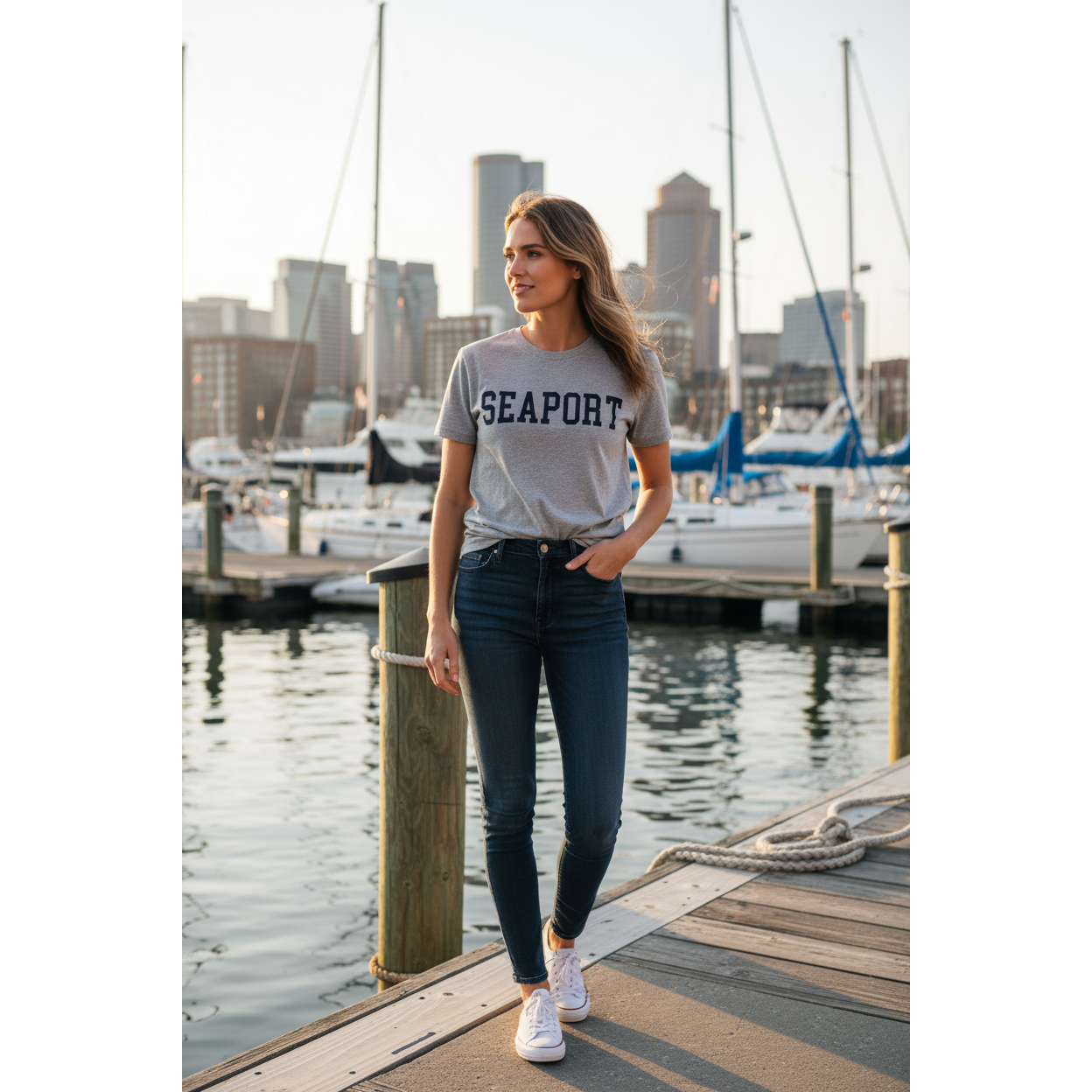 Woman at city marina wearing a gray short-sleeve T-shirt with 'SEAPORT' embroidered in dark letters on the front.