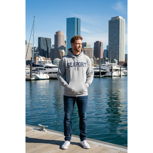 Man on boston harbor wearing a gray hoodie sweatshirt with 'SEAPORT' embroidered on the front