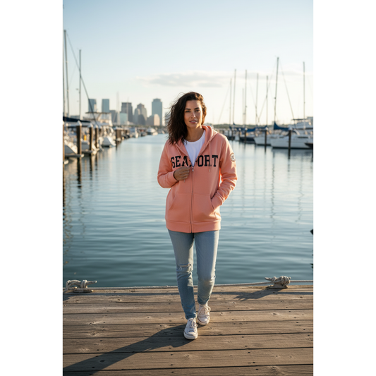 Woman on marina wearing peach lightweight full-zip hoodie with the word 'SEAPORT' embroidered on the chest and a logo on the left sleeve
