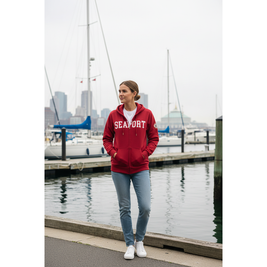 Woman at city marina a red lightweight full-zip hoodie with the text 'SEAPORT' written across the front, a visible brand logo, and a patch on the left shoulder.