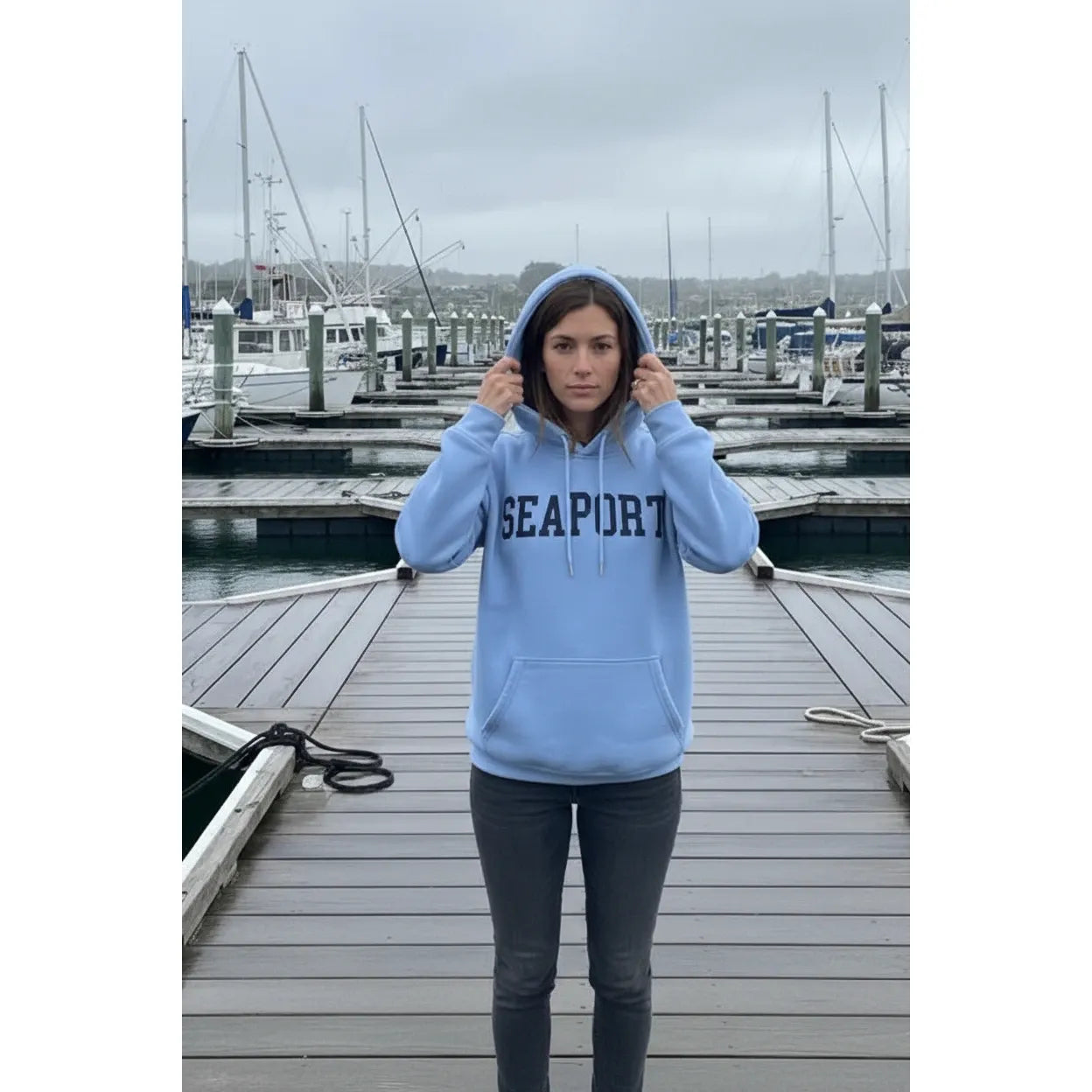 Person wearing a light blue heavy hoodie with 'SEAPORT' text, standing on a waterfront marina